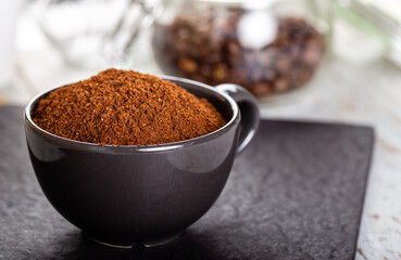 Black cup with ground coffee. Roasted coffee beans.