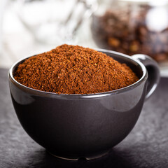 Black cup with ground coffee. Roasted coffee beans.