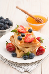 Photo of fresh homemade food made of Belgian waffles with honey, chocolate, strawberry, blueberry. Healthy dessert breakfast concept. 