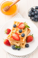 Photo of fresh homemade food made of Belgian waffles with honey, chocolate, strawberry, blueberry. Healthy dessert breakfast concept. 