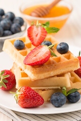 Photo of fresh homemade food made of Belgian waffles with honey, chocolate, strawberry, blueberry. Healthy dessert breakfast concept. 