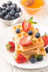 Photo of fresh homemade food made of Belgian waffles with honey, chocolate, strawberry, blueberry. Healthy dessert breakfast concept. 