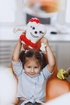 Cute little girl playing with knitted tooth toy while sitting on chair in dentist office
