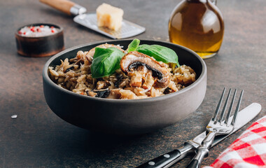 Traditional italian risotto with mushrooms and parmesan cheese on a dark bowl on a black table.