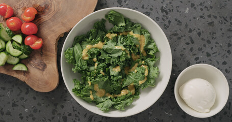 Top view massaged kale leaves in white ceramic bowl on concrete background