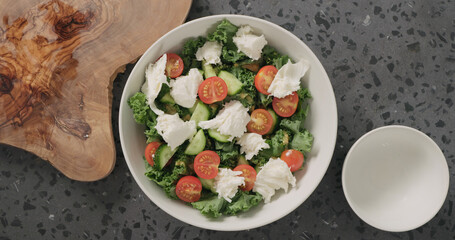 Top view add mozzarella over kale leavesand tomatoes in white ceramic bowl on concrete background