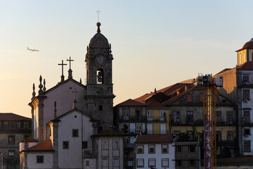 Fototapeta na wymiar View to the Paroquial de Nossa Senhora da Vitória church. Plane preparing for landing in the background. Sunset. Porto, Portugal