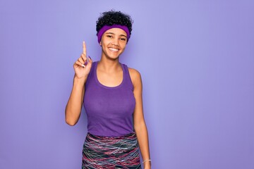 Beautiful african american afro woman wearing casual sportswear over purple background showing and pointing up with finger number one while smiling confident and happy.