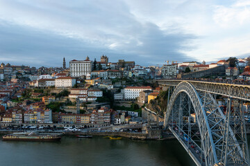 Fototapeta na wymiar Porto (Portugal) view, with Dom Luís Bridge and metro. Sunset, cloudy sky. Boats on the river.