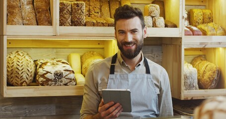 Portrait of happy baker working in bakery shop and using digital tablet computer.