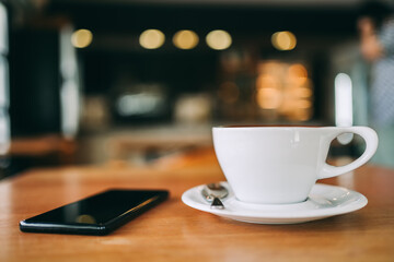 Close up a white cup of coffee in cafe, Selective focus on hand with copy space, blur background with bokeh in the warm morning