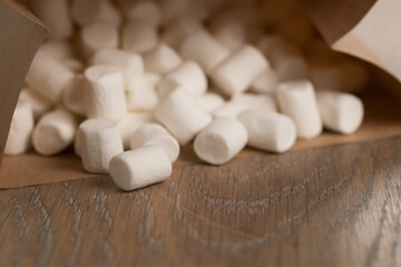 Fototapeta na wymiar small white marshmallows spilling from paper bag on wooden background