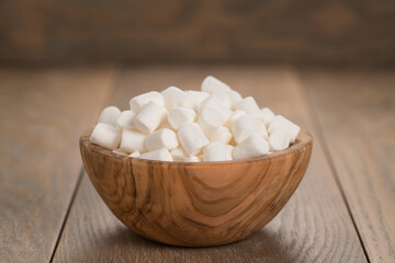 Fototapeta na wymiar small white marshmallows in olive bowl on wooden background