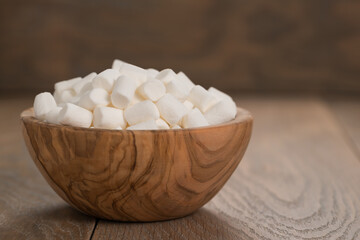 small white marshmallows in olive bowl on wooden background