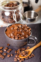Ground coffee in a black cup, and at the top several roasted coffee beans.