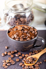 Ground coffee in a black cup, and at the top several roasted coffee beans.
