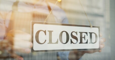 Close up of the male Caucasian hands turning a signboard on the glass door of the shop from CLOSED to OPEN and man in glasses looking out on the street.