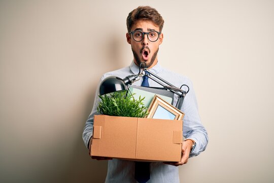 Young businessman with beard fired holding cardboard standing over white background scared in shock with a surprise face, afraid and excited with fear expression