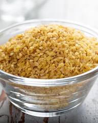 Uncooked bulgur in blue bowl on wooden table background. Dry bulgur. Spilled bulgur