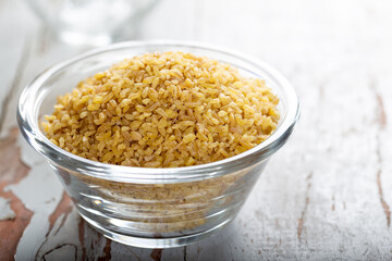 Uncooked bulgur in blue bowl on wooden table background. Dry bulgur. Spilled bulgur