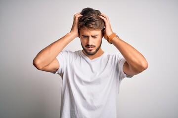 Young handsome man with beard wearing casual t-shirt standing over white background suffering from headache desperate and stressed because pain and migraine. Hands on head.