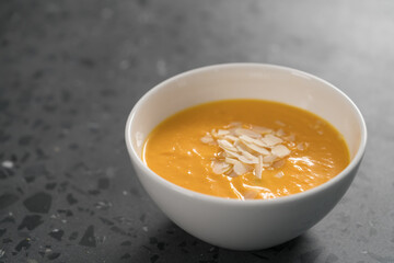 Pumpkin soup puree decorated with almond flakes in white bowl on concrete background