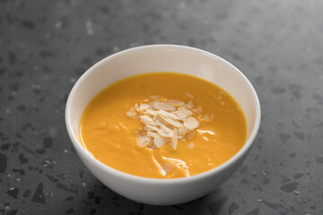 Pumpkin soup puree decorated with almond flakes in white bowl on concrete background