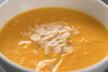Pumpkin soup puree decorated with almond flakes in white bowl closeup