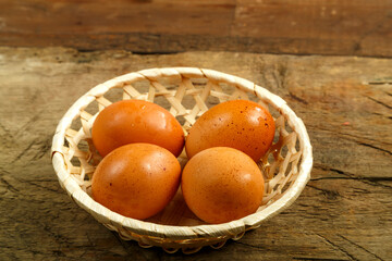 Chicken eggs in a wicker plate on a wooden table.