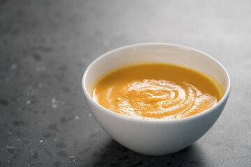 Pumpkin spicy soup puree in white bowl on concrete background
