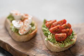 Bruschettas with avocado, tomato and mozzarella on wood board on concrete bacground