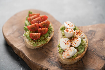 Bruschettas with avocado, tomato and mozzarella on wood board on concrete bacground
