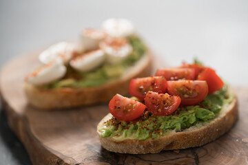 Bruschettas with avocado, tomato and mozzarella on wood board on concrete bacground