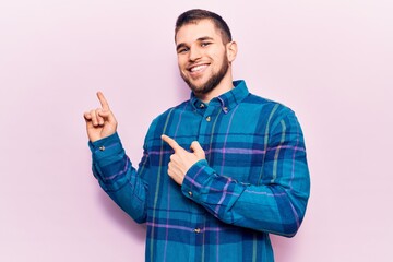 Young handsome man wearing casual shirt smiling and looking at the camera pointing with two hands and fingers to the side.