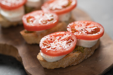 Bruschetta with tomatoes, mozzarella and pesto on olive wood board