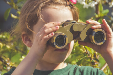 child girl looking through binoculars on a background of flowers