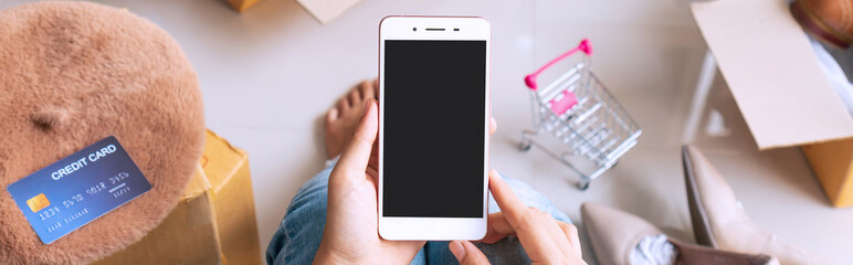 Hands of women holding smartphone with credit card, postal parcel on the floor. Online shopping, e-commerce, online financial management concept. Top view, copy space