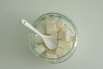 Refined sugar and a white spoon in a glass jar on a white table. The view from the top
