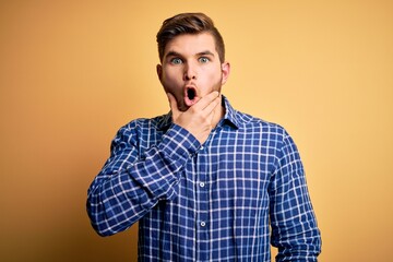 Fototapeta premium Young blond businessman with beard and blue eyes wearing shirt over yellow background Looking fascinated with disbelief, surprise and amazed expression with hands on chin