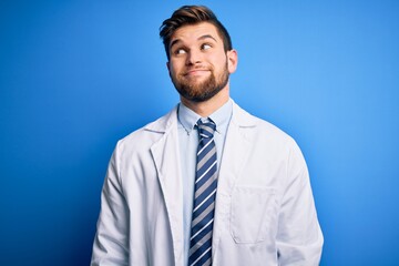 Young blond therapist man with beard and blue eyes wearing coat and tie over background smiling looking to the side and staring away thinking.