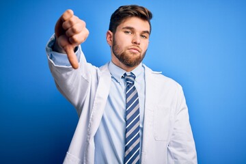 Young blond therapist man with beard and blue eyes wearing coat and tie over background looking unhappy and angry showing rejection and negative with thumbs down gesture. Bad expression.