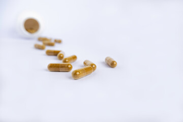 Mustard color capsules with turmeric (curcuma) close-up on a light background lie near a plastic jar of vitamins