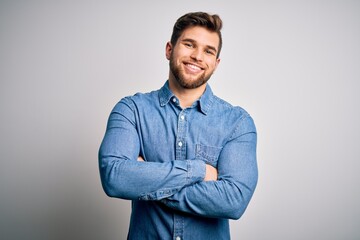 Young handsome blond man with beard and blue eyes wearing casual denim shirt happy face smiling with crossed arms looking at the camera. Positive person.