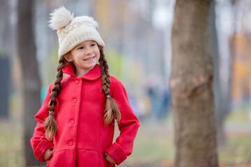 Beautiful little girl in red coat outdoors in a autumn park.