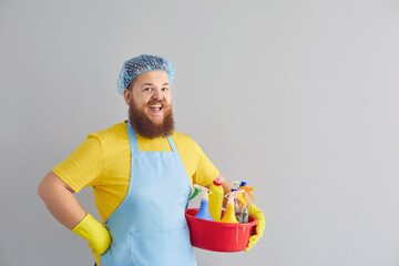 Funny fat man with a beard in an apron cleans up on a gray background.