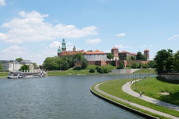 Fototapeta na wymiar Landscape with Vistula river and Wawel Royal Castlee. People walking and cycling along path by river on sunny summer day. Cracow, Poland.