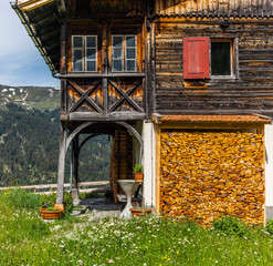 Old traditional wood chalet on the alpine meadows covered in green grass and colorful flowers in...