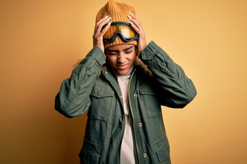 Young african american afro skier girl wearing snow sportswear and ski goggles suffering from headache desperate and stressed because pain and migraine. Hands on head.