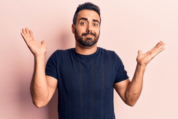Naklejka premium Young hispanic man wearing casual clothes clueless and confused with open arms, no idea and doubtful face.