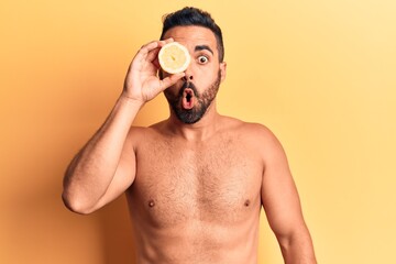 Young hispanic man standing shirtless holding lemon scared and amazed with open mouth for surprise, disbelief face